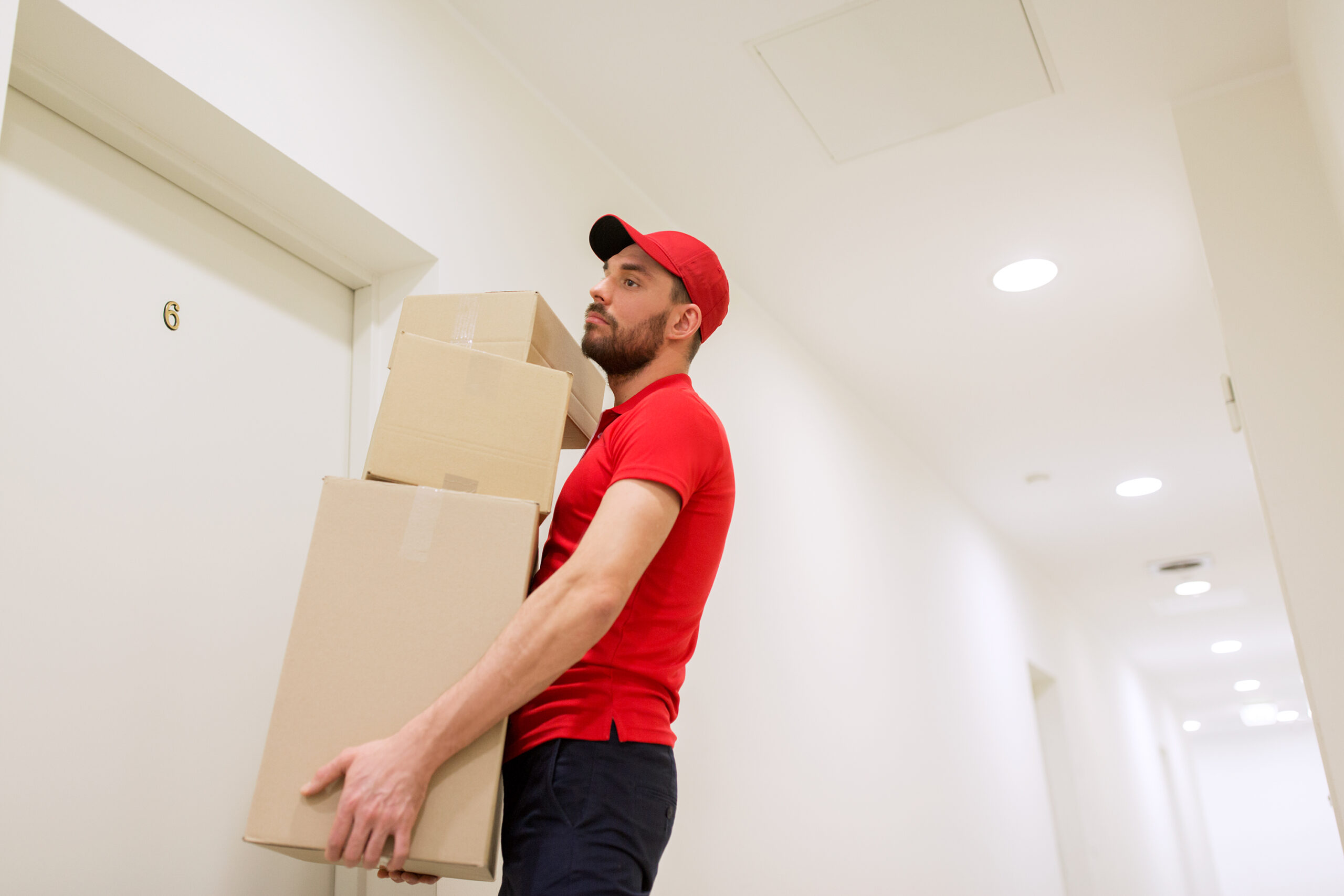 delivery, mail, people and shipment concept - man in red uniform with parcel boxes in corridor at customer door
